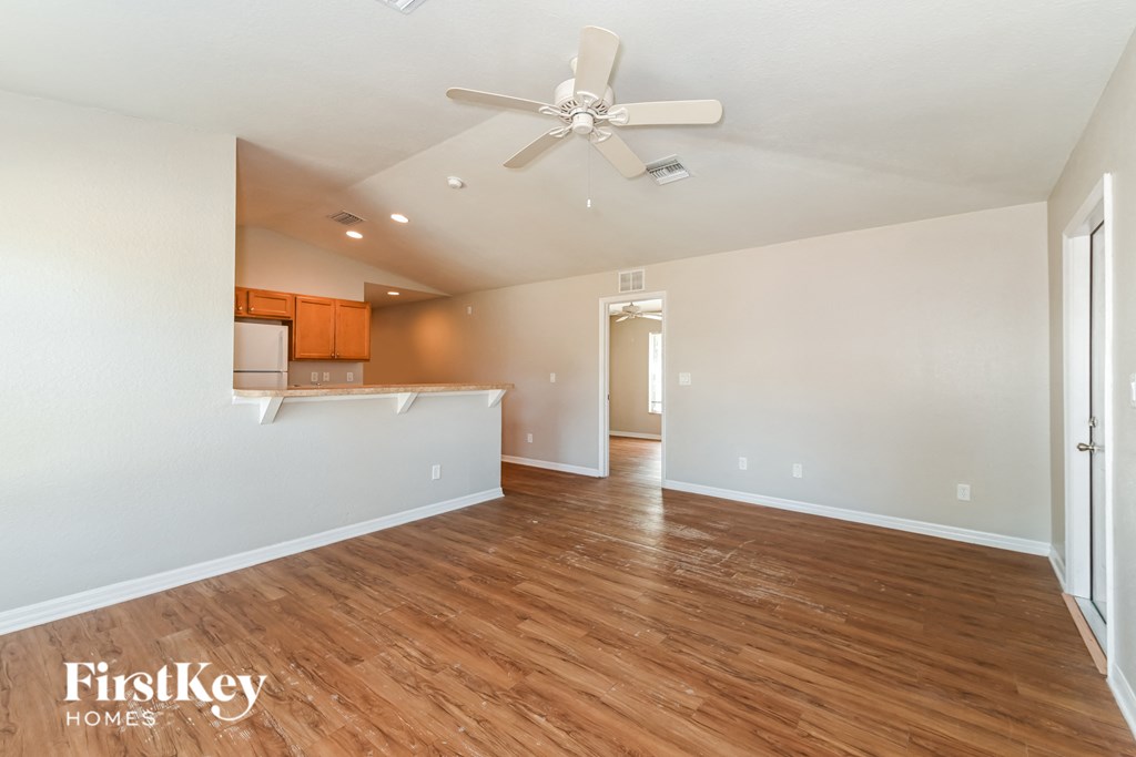 an empty living room with a ceiling fan and a kitchen