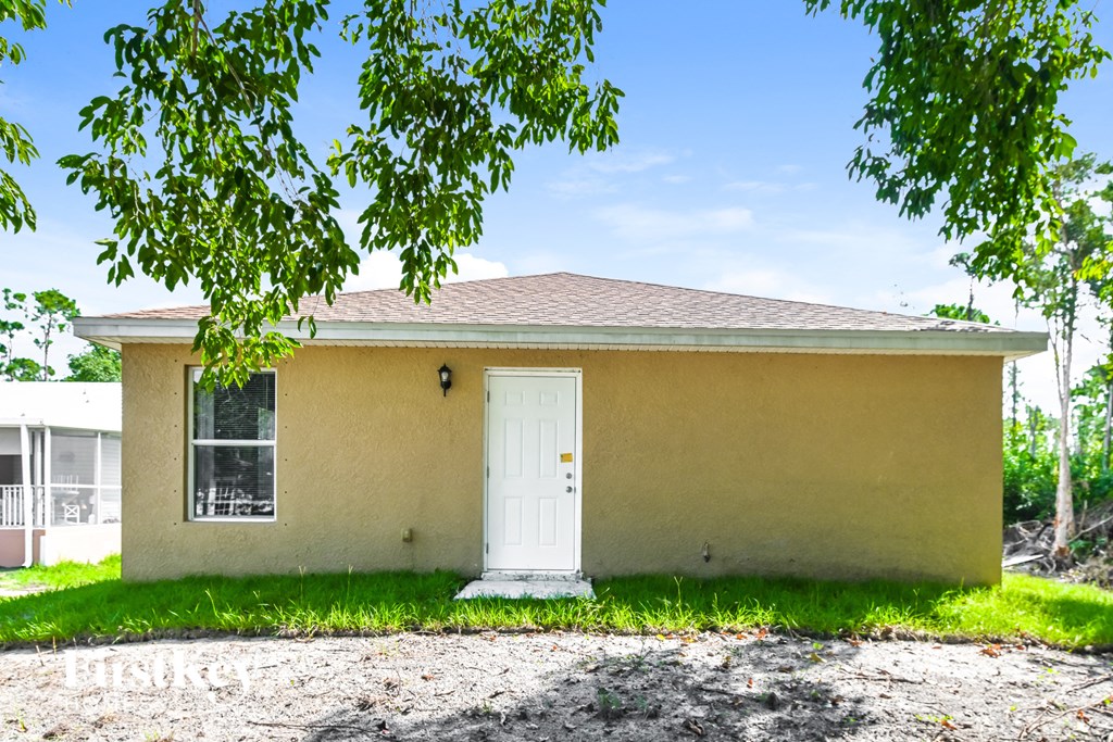 a small tan house with a white door and a tree