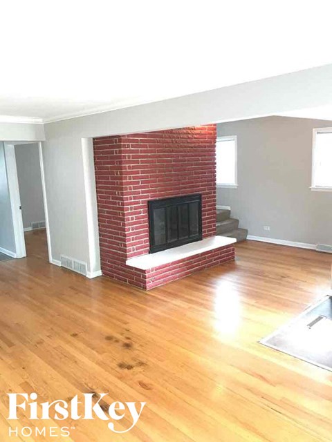 an empty living room with a brick fireplace and wooden floors