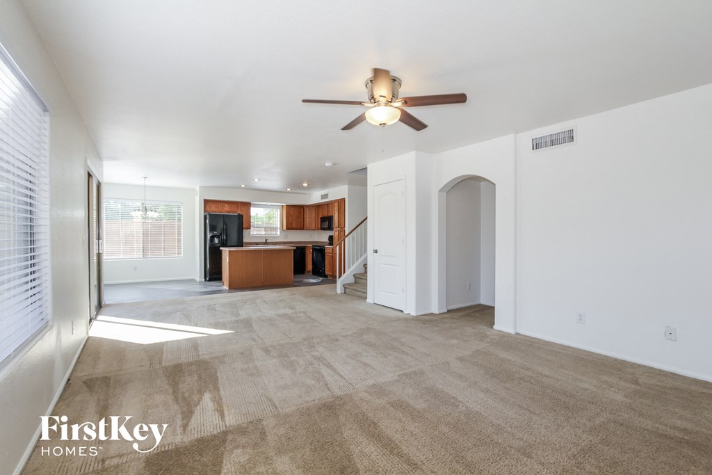 A spacious living room with a carpeted floor and a ceiling fan.
