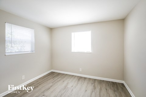 a bedroom with wood flooring and two windows