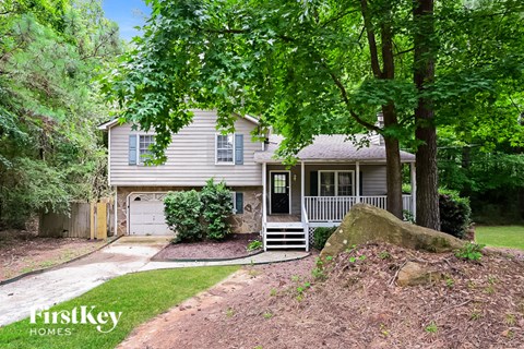 A house with a grey roof and a white fence is surrounded by green trees.