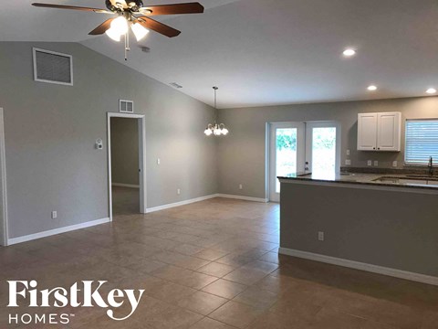 A spacious room with a ceiling fan and a kitchen area in the background.