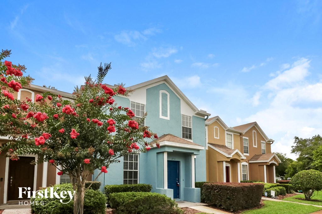 A house with a blue door and a tree with red flowers in front of it.