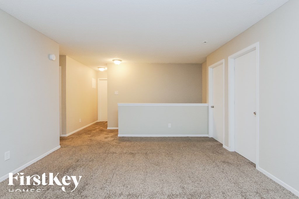 A spacious room with a carpeted floor and white walls, with a white door on the right side.