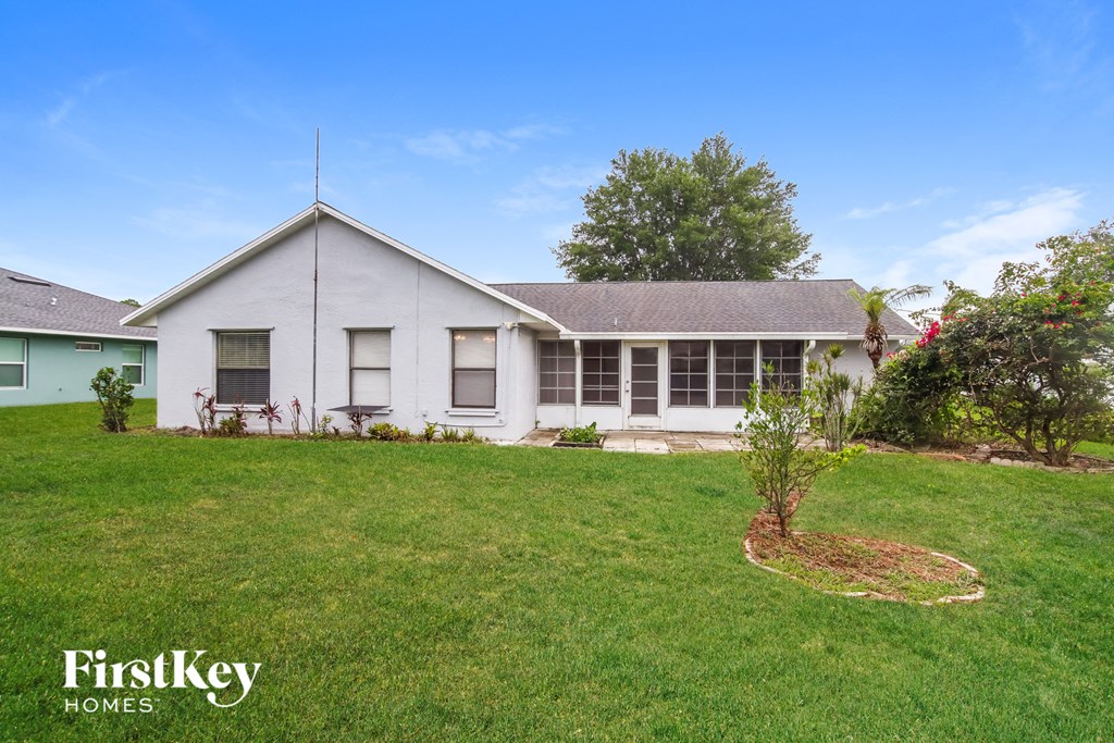 the front of a white house with a lawn and a tree