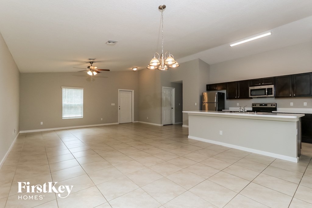 an empty living room with a kitchen and a ceiling fan