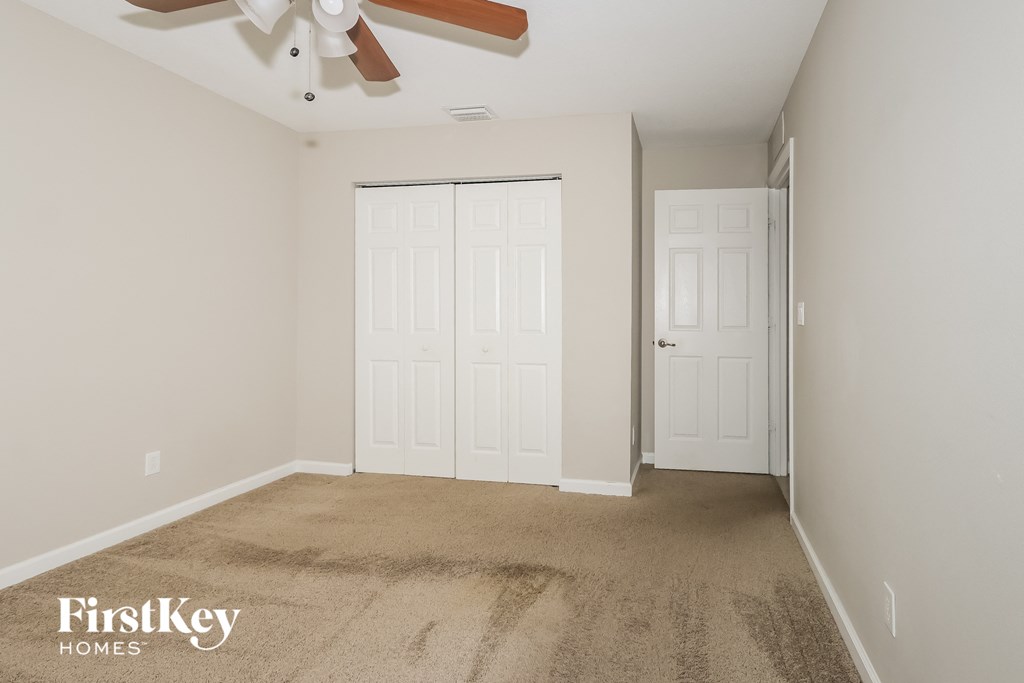 a clean carpeted room with two doors and a ceiling fan