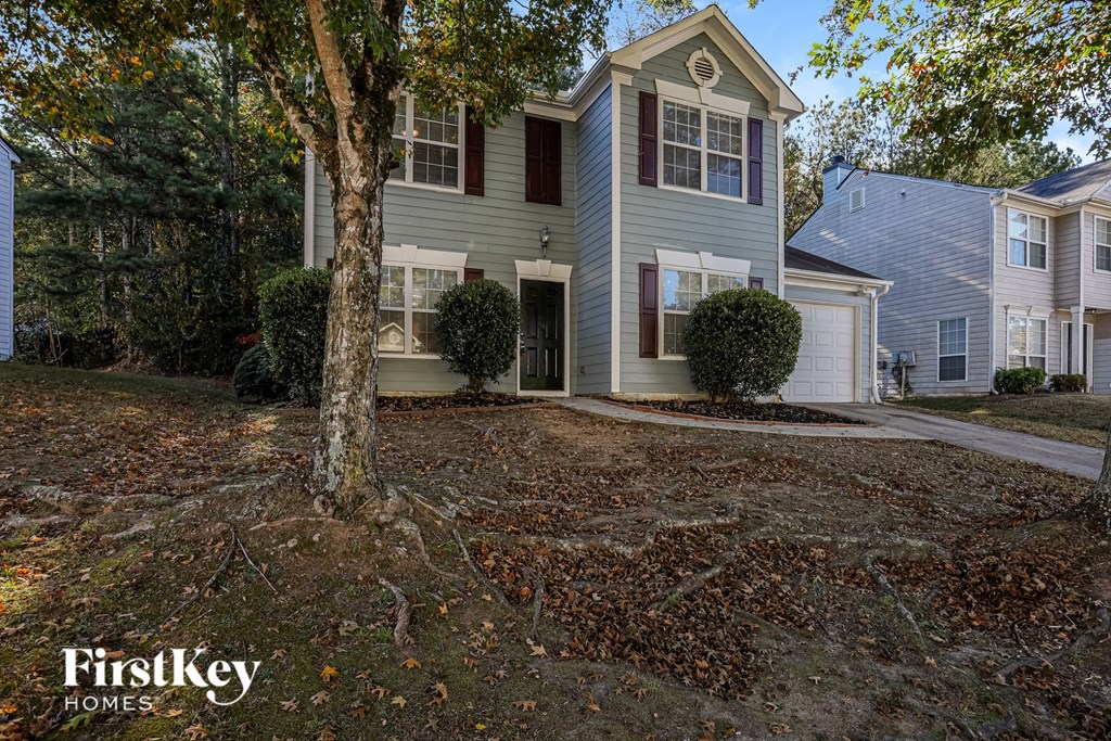 A tree stands in front of a grey house with a white door.