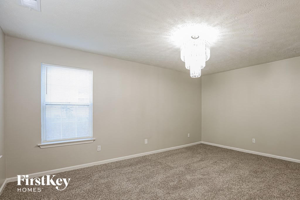 A room with a carpet floor, a window with blinds, and a chandelier.