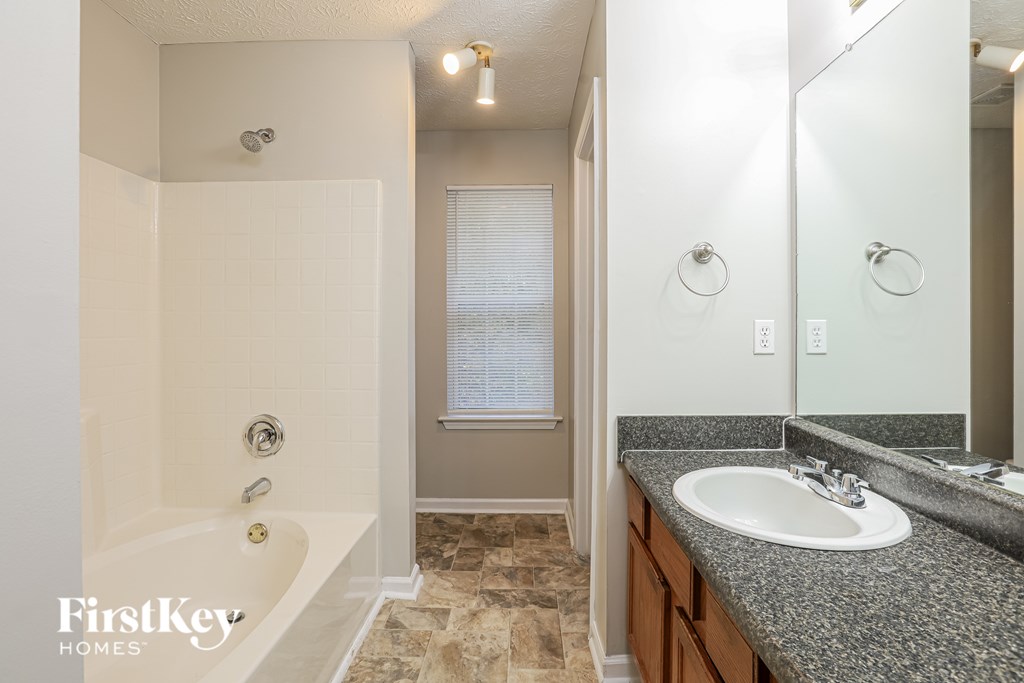 A bathroom with a tub, sink and mirror.