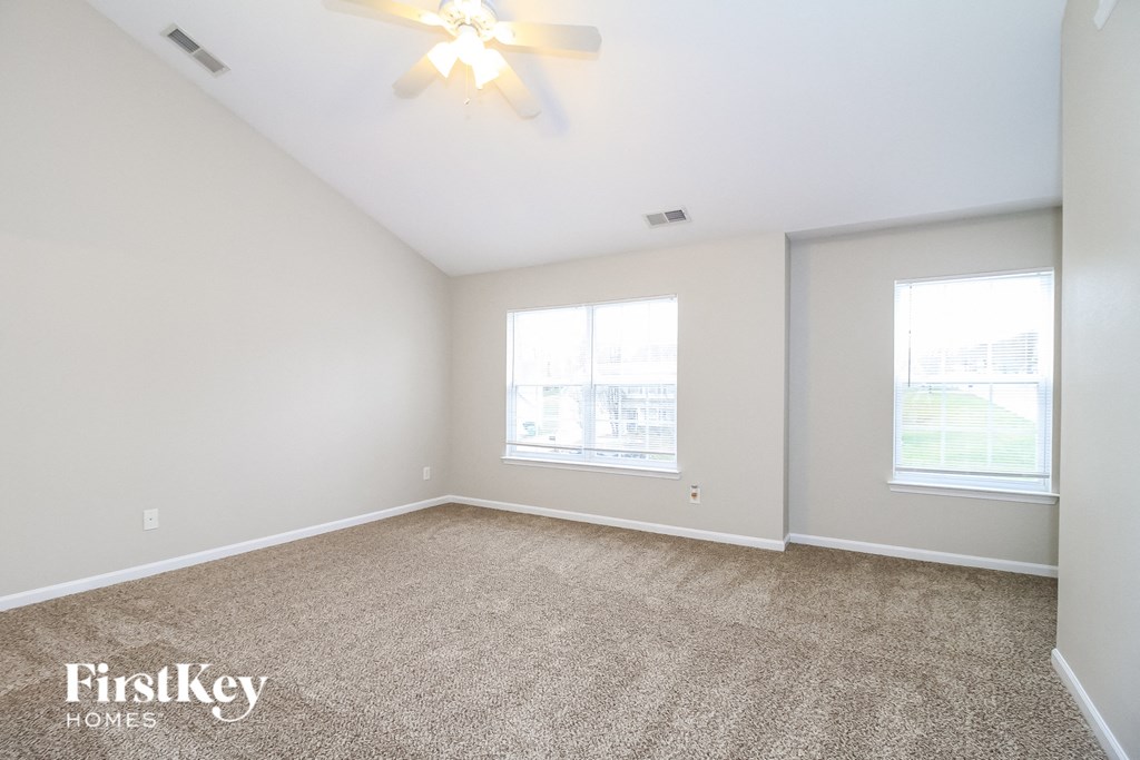 the living room of an apartment with carpet and a ceiling fan