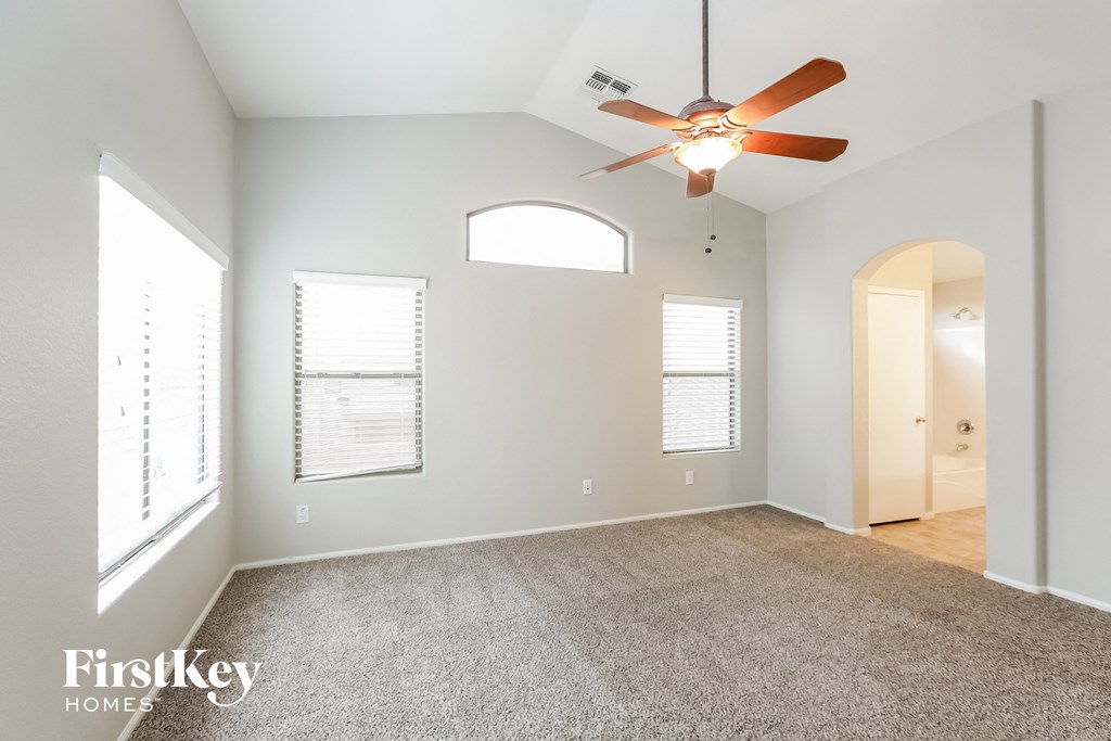 an empty living room with a ceiling fan and a door to a hallway