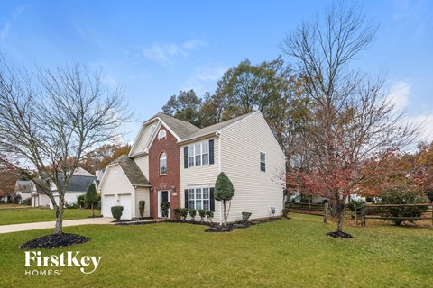 A house with a red brick chimney and a white exterior is surrounded by a grassy lawn and trees.
