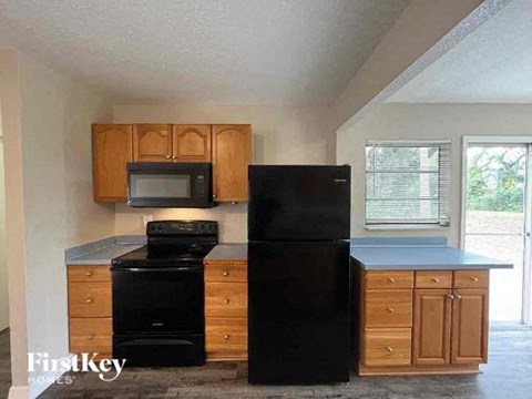 A black refrigerator stands next to a black oven and microwave in a kitchen.