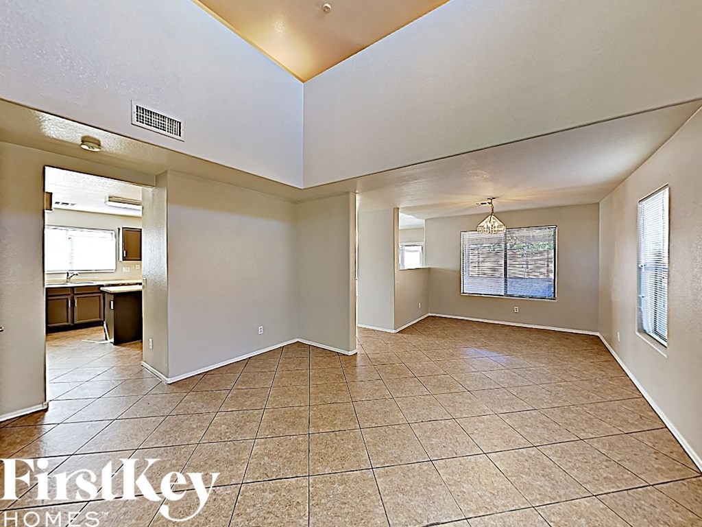 an empty living room with tile flooring and a kitchen