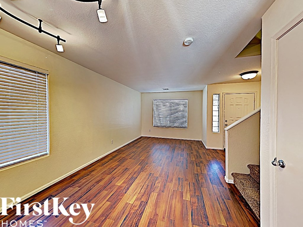 an empty living room with hardwood flooring and a door to the kitchen