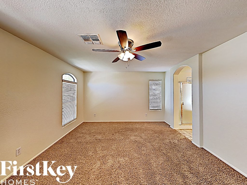 an empty living room with a ceiling fan and a door to a hallway