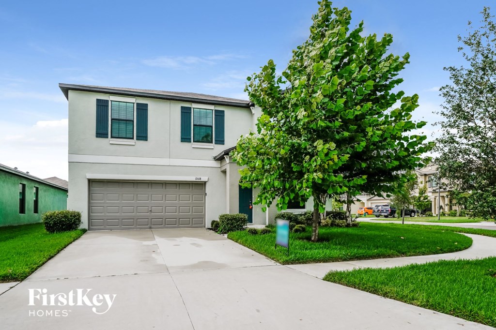 A white house with a green garage door and a tree in front.