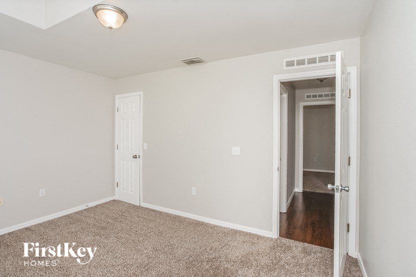a bedroom with white walls and carpet and a door to a hallway