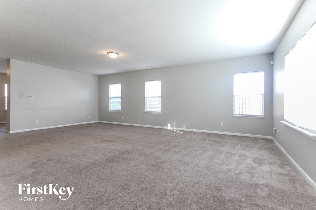 A spacious room with a carpeted floor and three windows.