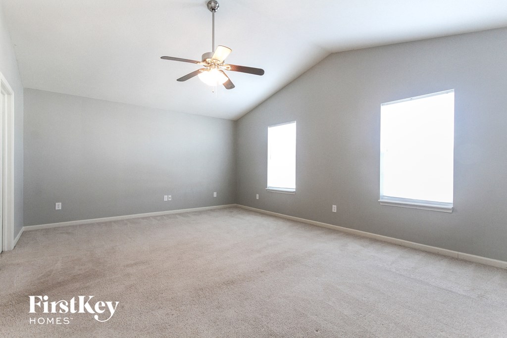 A spacious room with a ceiling fan and two windows.
