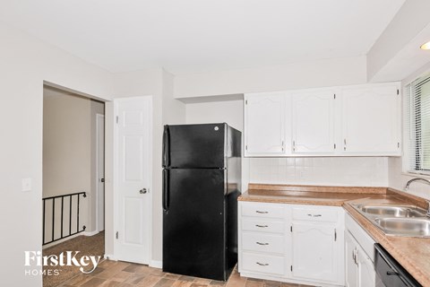 A black fridge in a kitchen with white cabinets.