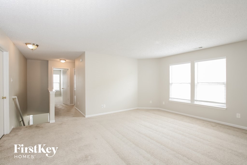 A spacious room with a carpeted floor and two windows.