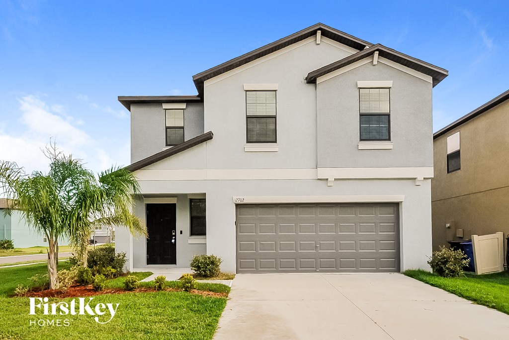 a white house with a garage door and a palm tree