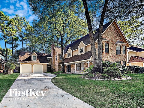 the front of a brick house with a driveway and trees