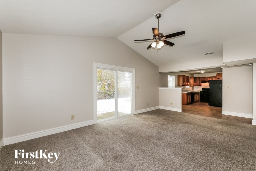an empty living room with a ceiling fan and a door to a kitchen