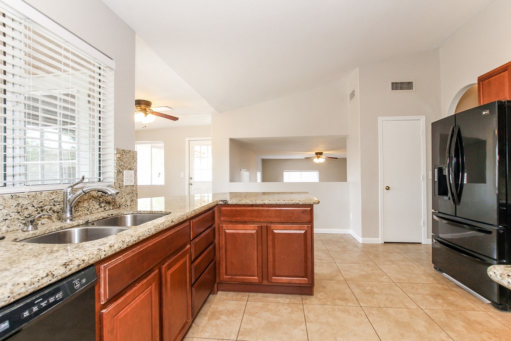 A kitchen with a black refrigerator and brown cabinets.