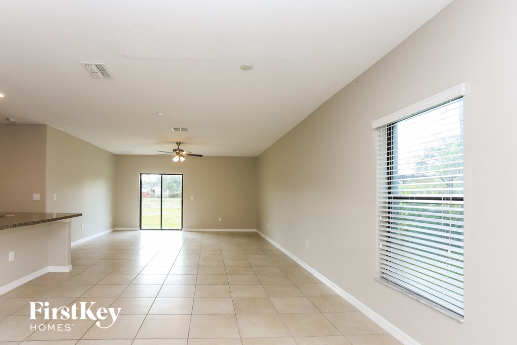 an empty living room with a large window and a ceiling fan