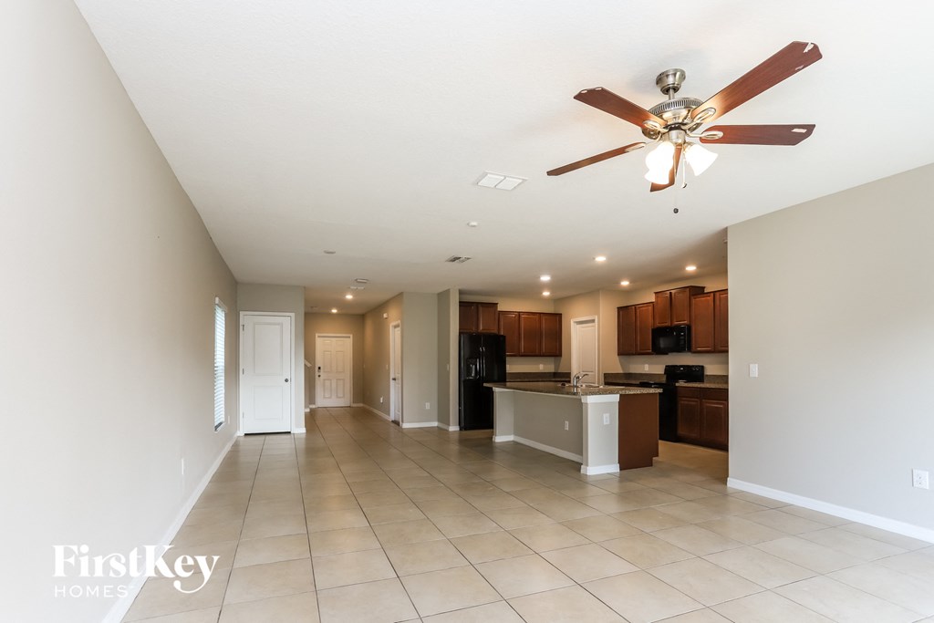 an empty living room with a ceiling fan and a kitchen