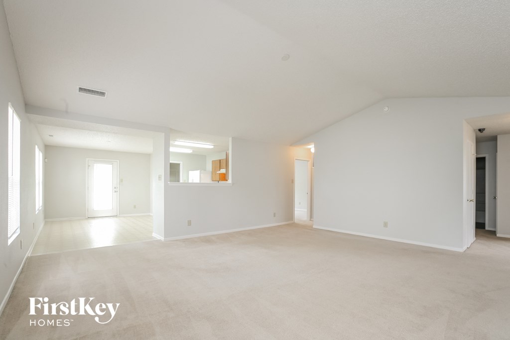 the living room and dining room of an apartment with white walls and flooring