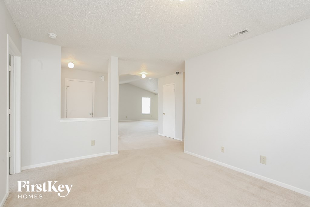 the living room and dining room of an apartment with white walls and carpet
