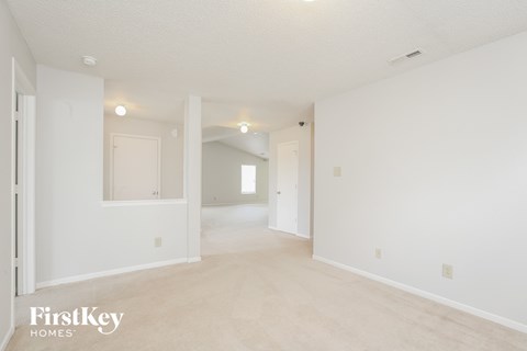 the living room and dining room of an apartment with white walls and carpet
