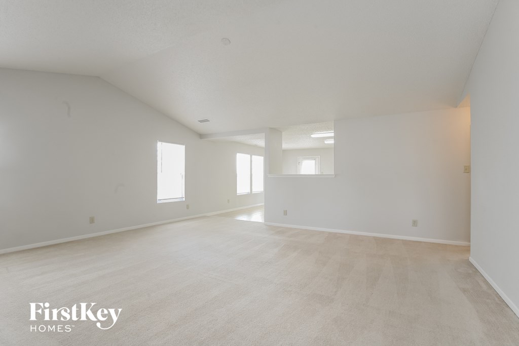the living room and dining room of an apartment with white walls and flooring