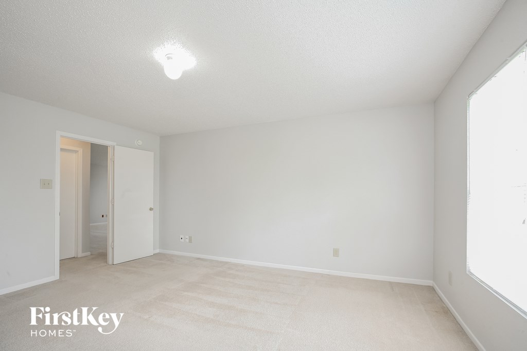 the living room and dining room of an apartment with white walls and carpet