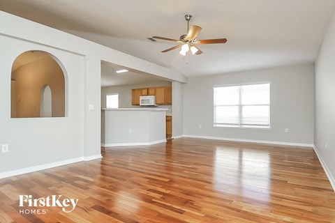 an empty living room with a ceiling fan and a kitchen
