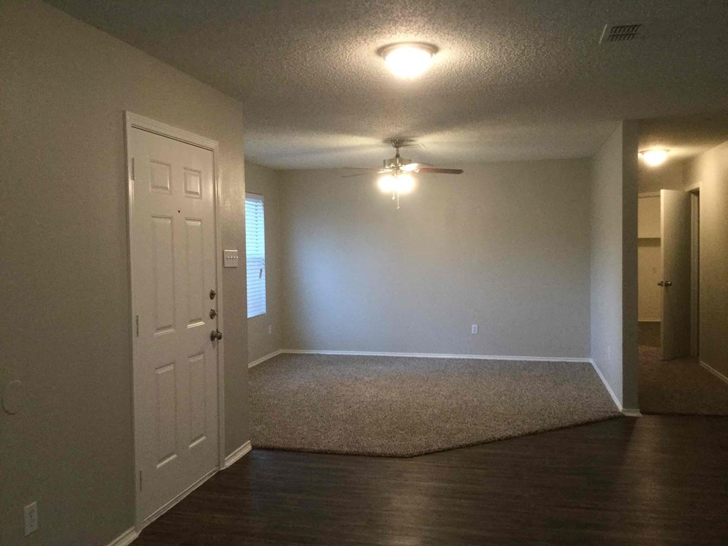 an empty living room with a white door and a ceiling fan