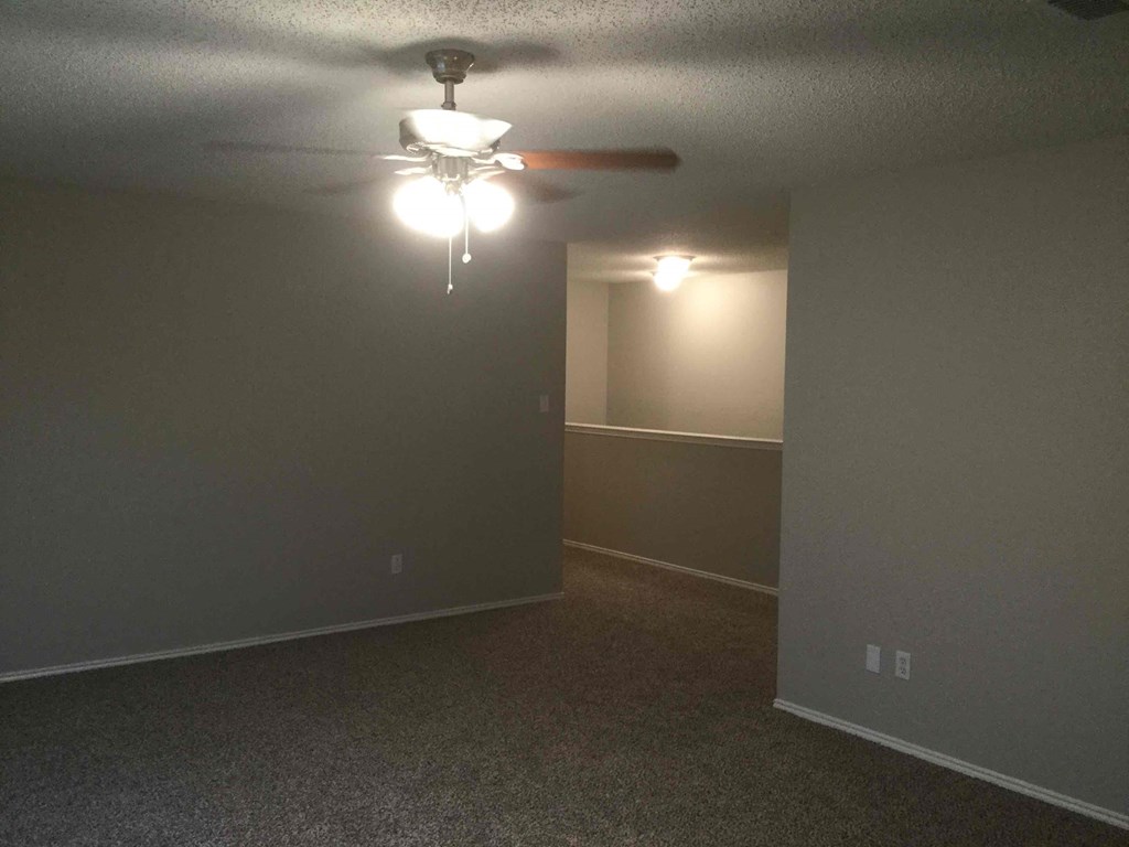 an empty living room with a ceiling fan and lights