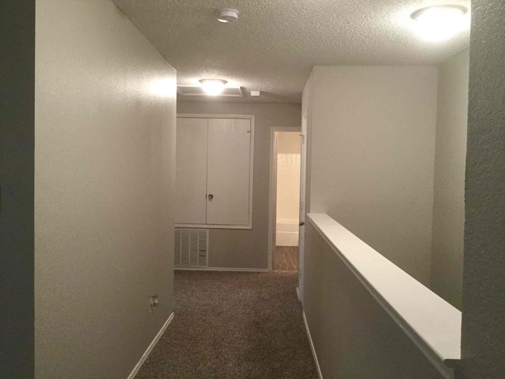 a hallway with white walls and a white railing and a closet