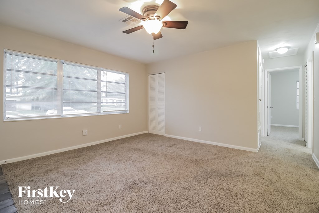 A room with a carpet floor, a ceiling fan, and a window with blinds.