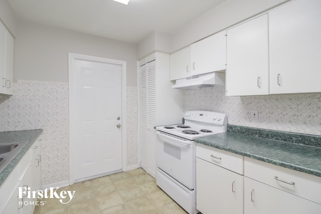 A kitchen with white cabinets and a white stove top oven.