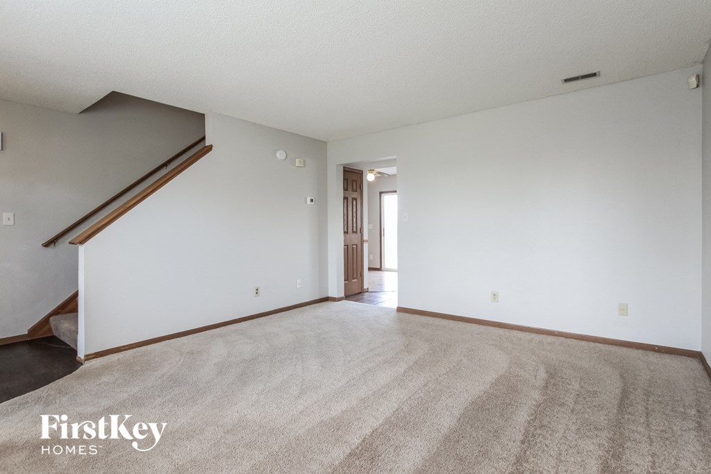 the living room and dining room of an apartment with carpeting and white walls