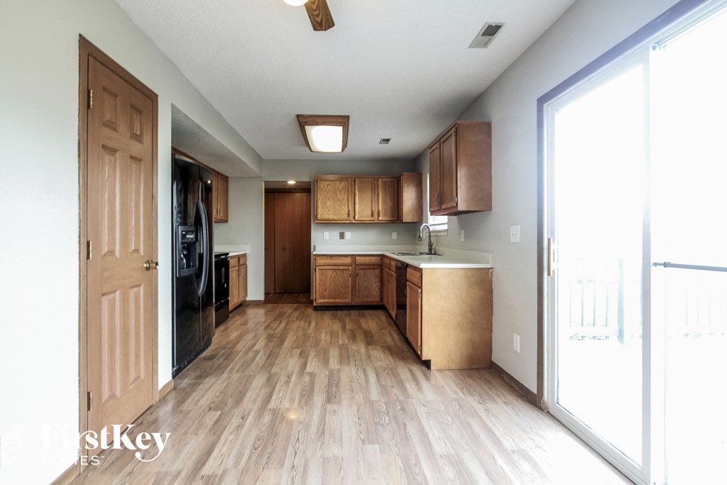 an empty kitchen with wood flooring and wooden cabinets and a large window