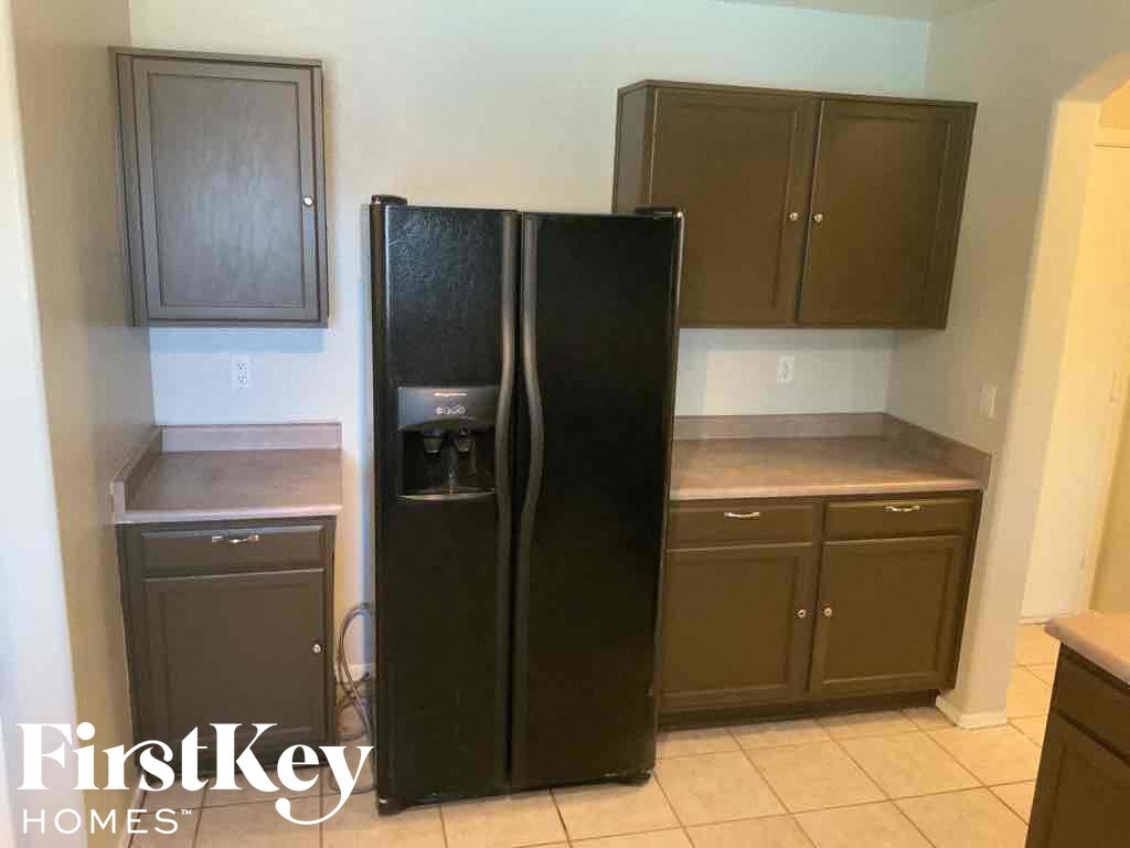 A black refrigerator stands in a kitchen with brown cabinets.