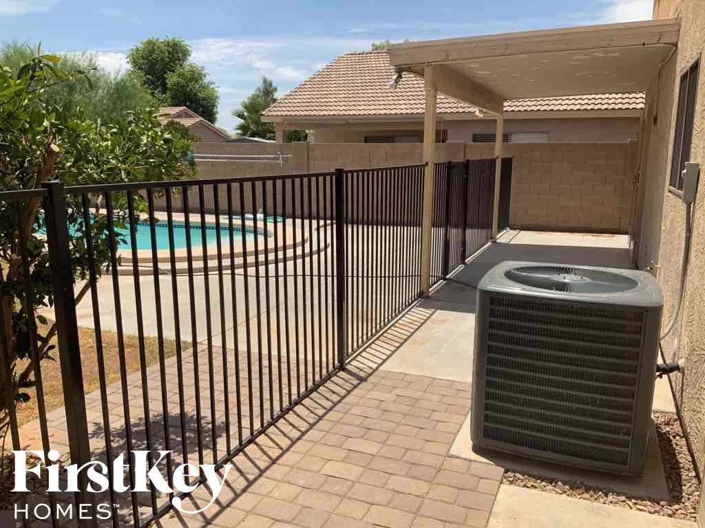 A black gate surrounds a pool and leads to a patio with a black air conditioning unit.