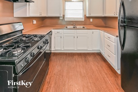 A kitchen with a black refrigerator and wooden floors.